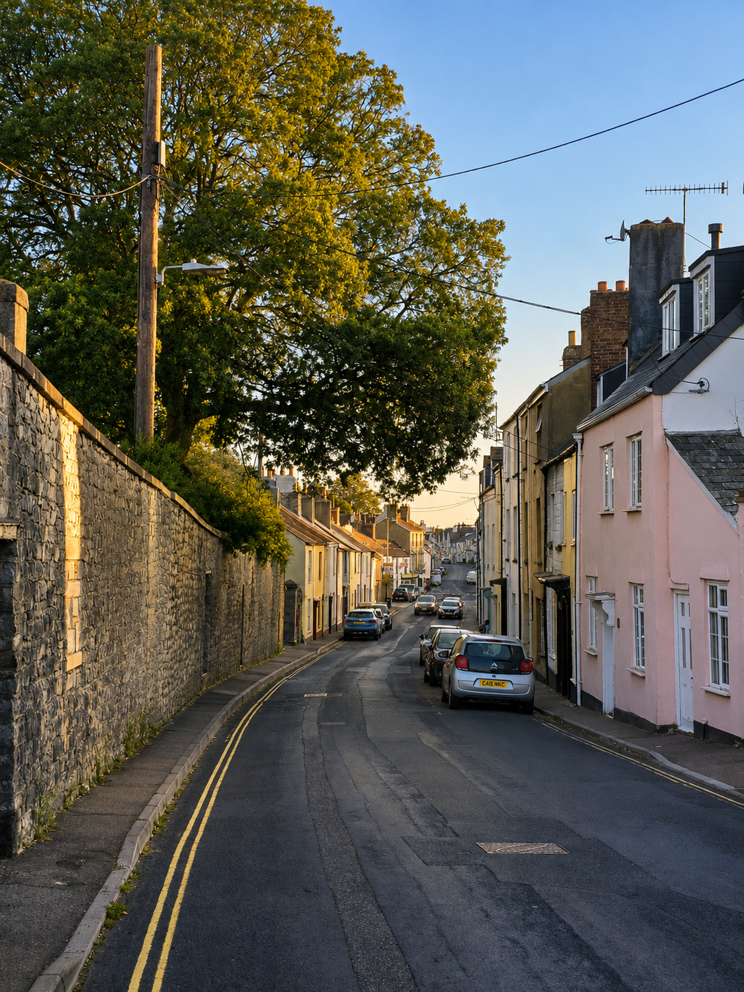 Fore Street in Chudleigh, Devon at golden hour, with stone walls and pastel cottages sloping down the hill